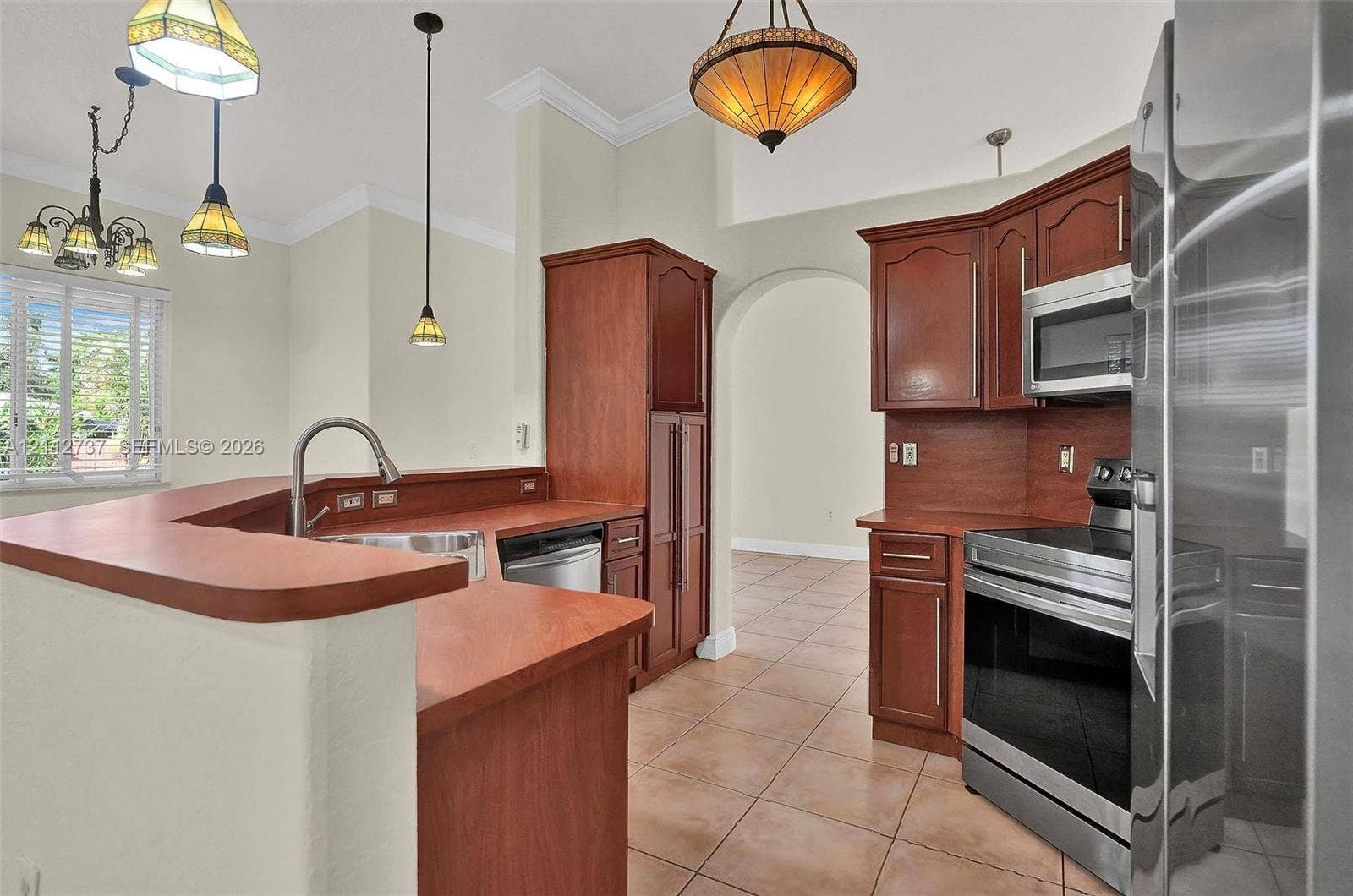 27902 SW 159th Court, Homestead, FL 33031 Kitchen featuring wooden cabinetry, stainless steel appliances, ceramic tile flooring, a wrap-around counter, and multi-light pendant fixtures