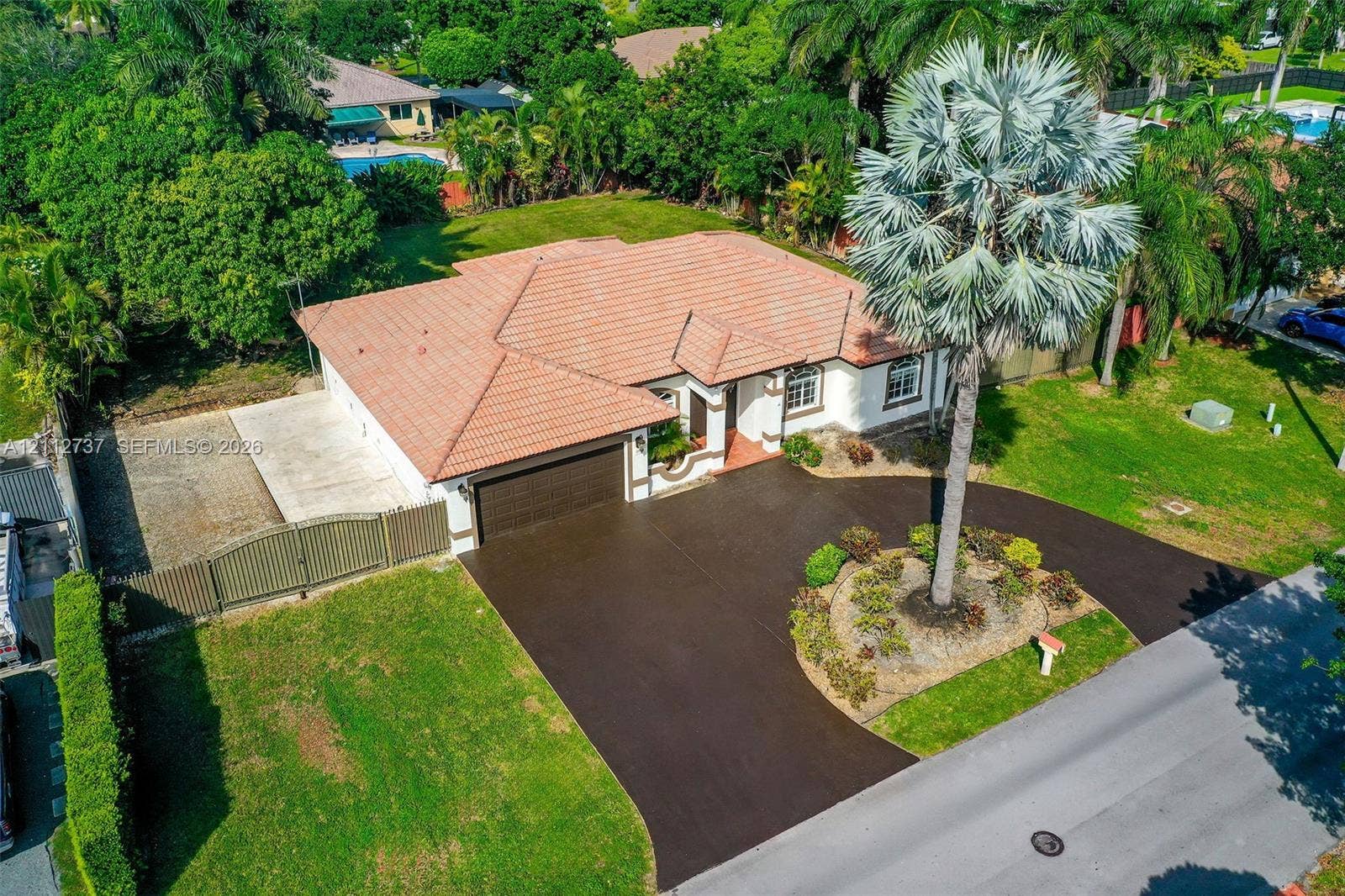 27902 SW 159th Court, Homestead, FL 33031 Single-story residence featuring a tiled roof, multi-car garage, expansive paved driveway, and established landscaping