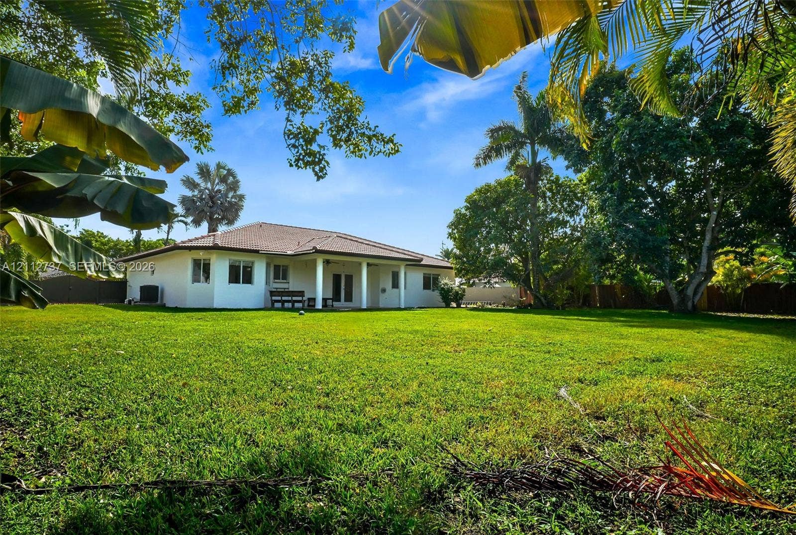 27902 SW 159th Court, Homestead, FL 33031 Expansive backyard featuring a sprawling lawn, mature tropical trees, and a covered rear patio