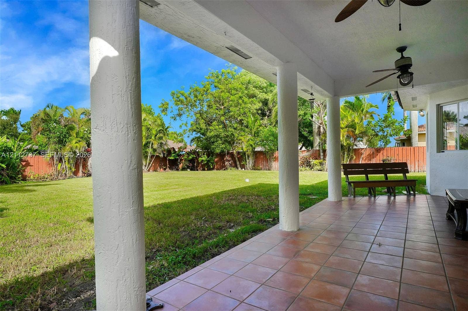 27902 SW 159th Court, Homestead, FL 33031 Covered patio featuring ceramic tile flooring, structural pillars, and ceiling-mounted fans overlooking a fenced backyard with mature trees