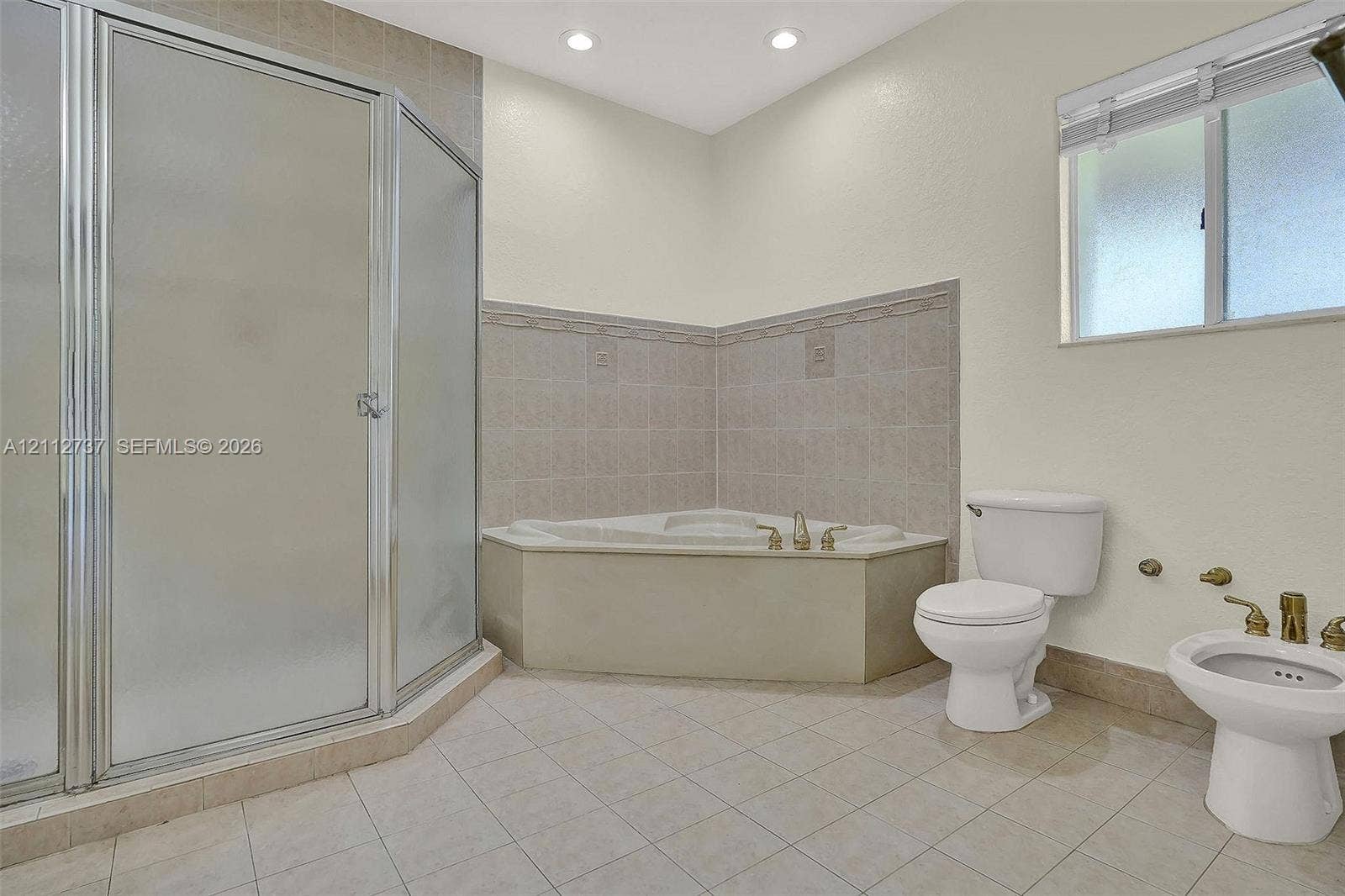 27902 SW 159th Court, Homestead, FL 33031 Corner soaking tub with tile surround, glass-enclosed shower, porcelain toilet, and bidet featuring metallic hardware