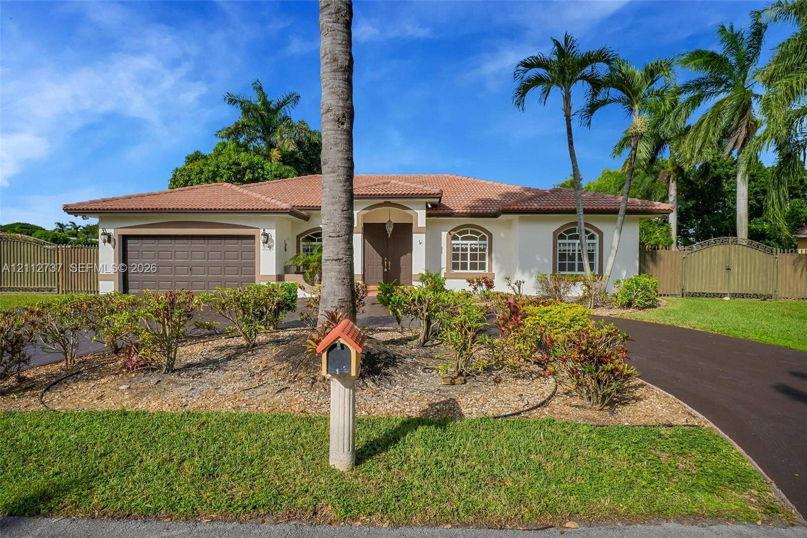 27902 SW 159th Court, Homestead, FL 33031 Single-story stucco exterior featuring a tile roof, arched windows, dual-car garage, and mature palm landscaping