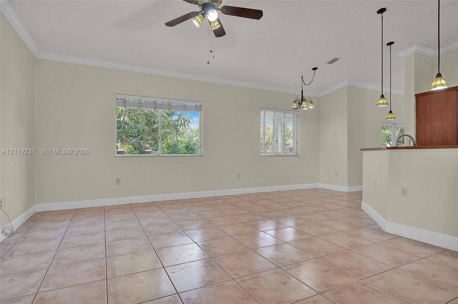 27902 SW 159th Court, Homestead, FL 33031 Open living area featuring large-format ceramic tile flooring, crown molding, a central ceiling fan with integrated lighting, and multiple pendant lights over a breakfast bar
