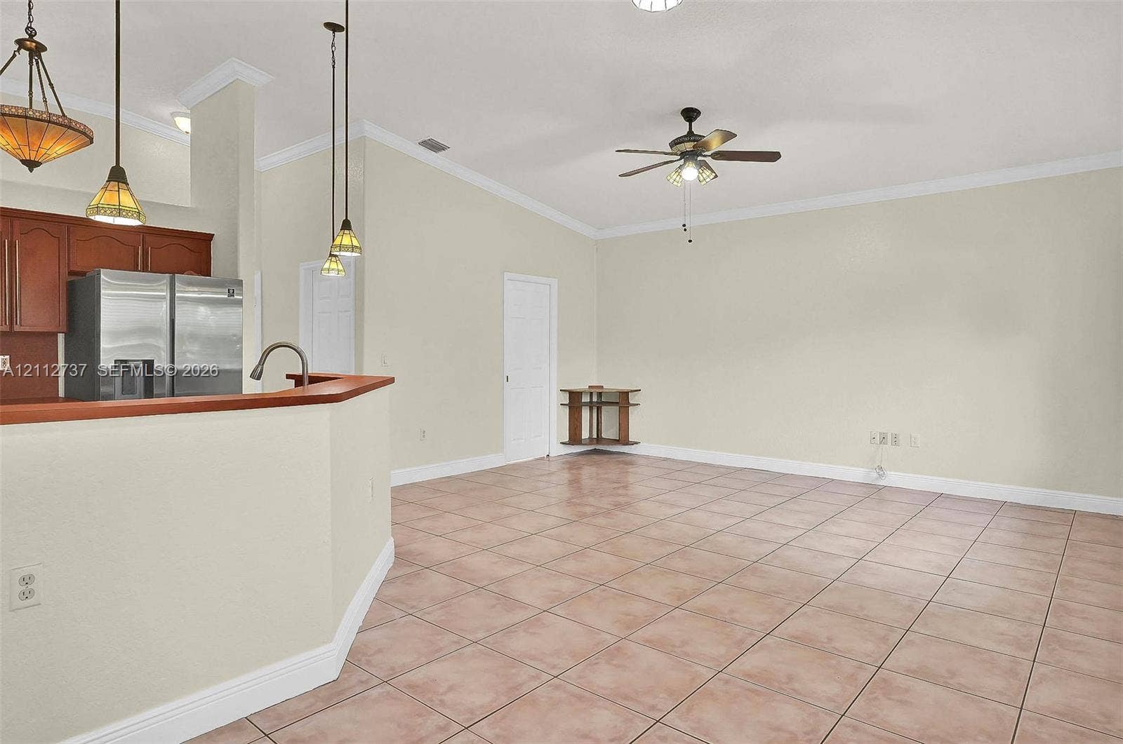 27902 SW 159th Court, Homestead, FL 33031 Open-concept space featuring tile flooring, vaulted ceilings with crown molding, a kitchen pass-through counter, pendant lighting, and a ceiling fan