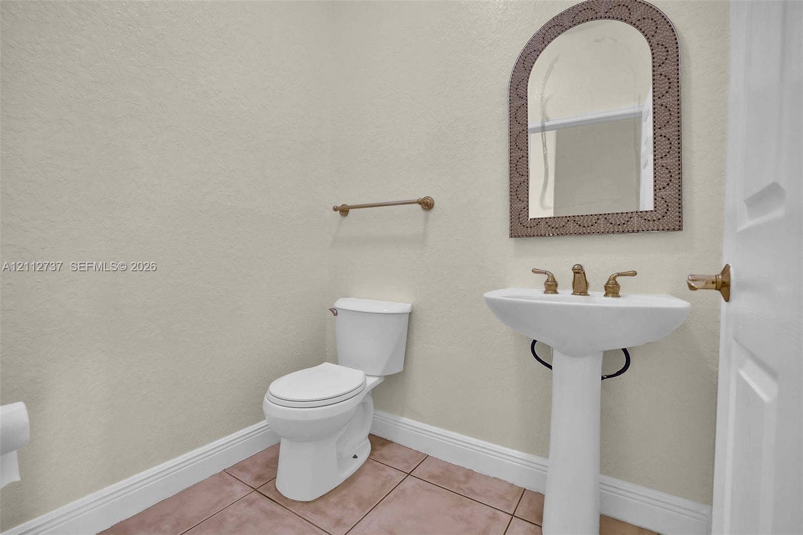 27902 SW 159th Court, Homestead, FL 33031 Pedestal sink with gold-tone hardware, arched wall mirror with decorative frame, neutral wall finishes, and tiled flooring