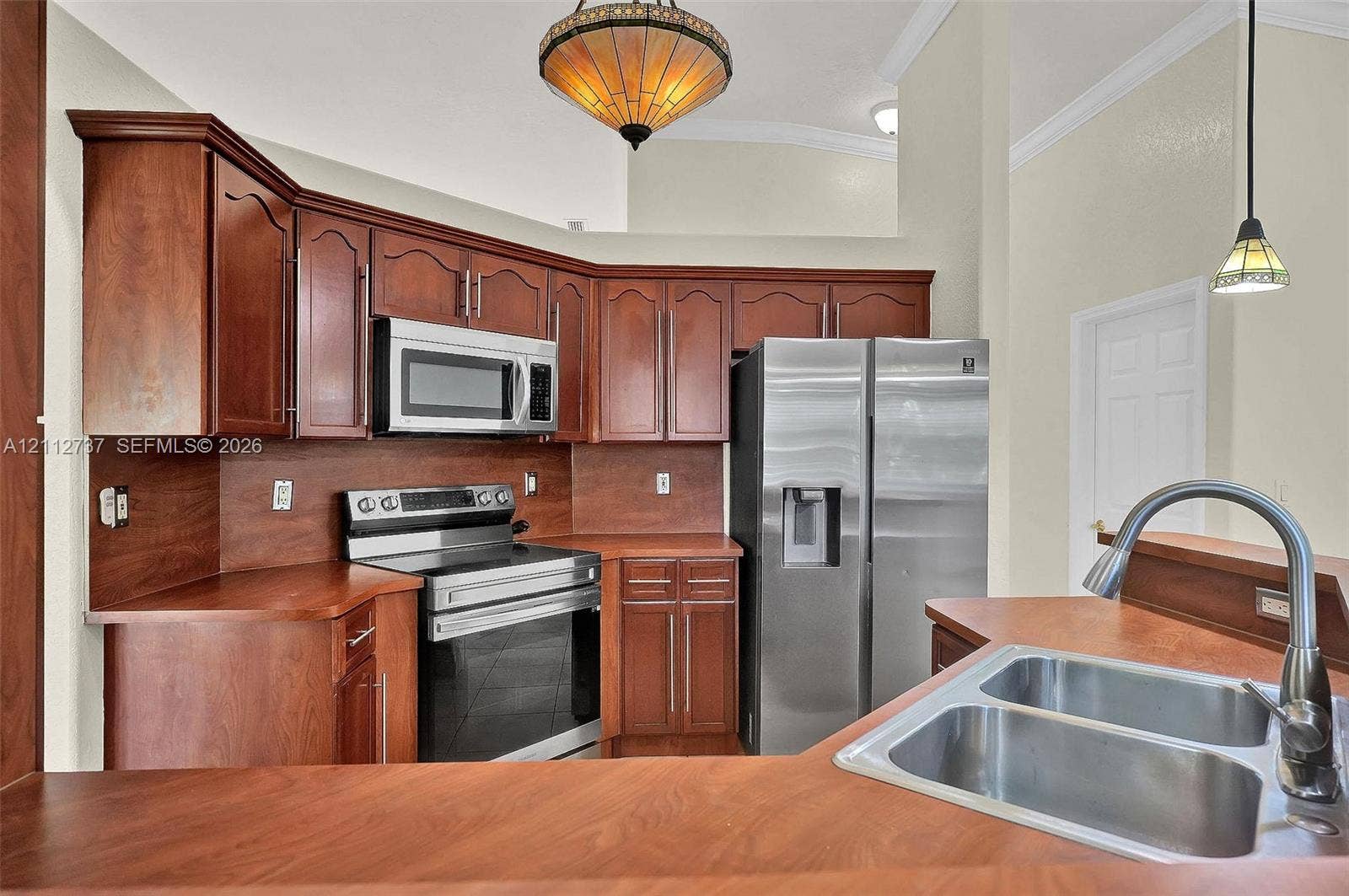 27902 SW 159th Court, Homestead, FL 33031 Kitchen featuring cherry-toned cabinetry, stainless steel appliances, a double-basin under-mount sink, high-vaulted ceilings, and multi-light pendant fixtures