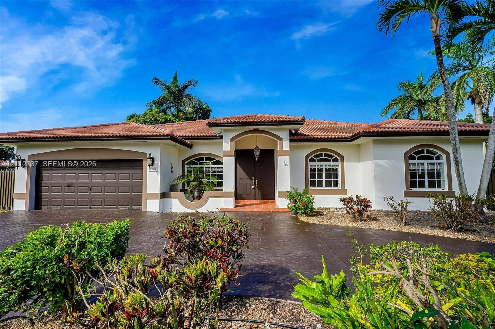 27902 SW 159th Court, Homestead, FL 33031 Stucco exterior featuring a tiled hip roof, arched window casings, double-door entryway, and a textured paver driveway