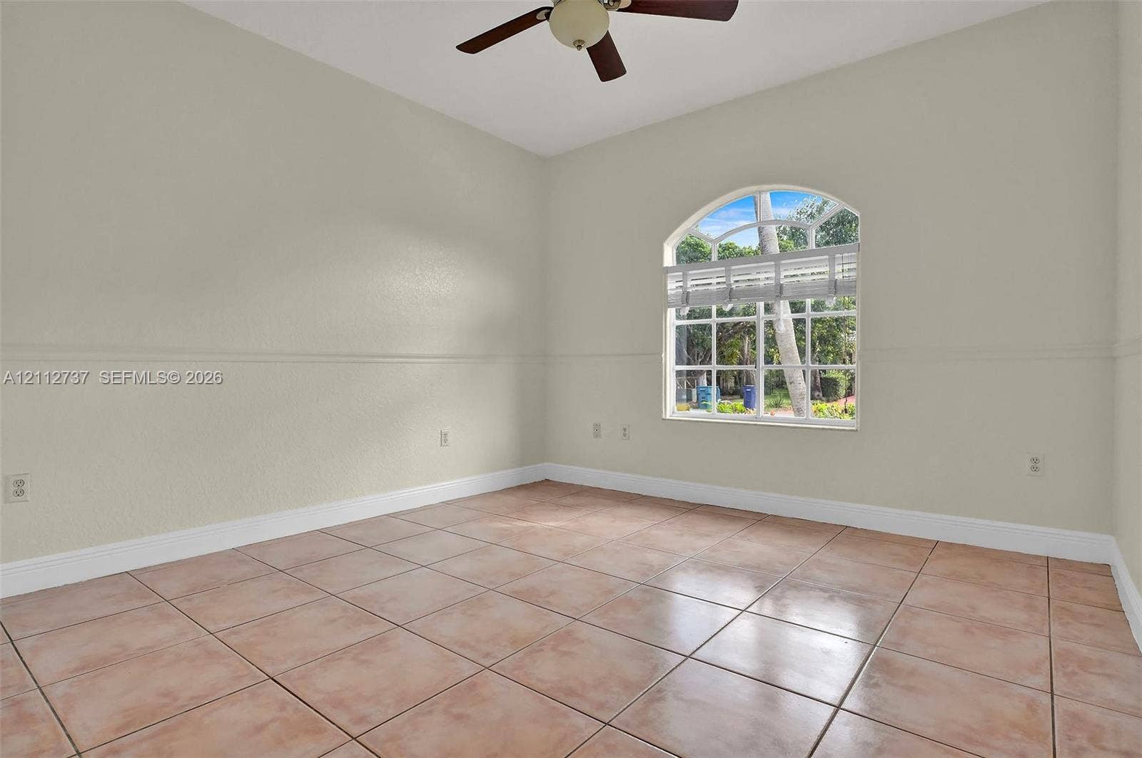27902 SW 159th Court, Homestead, FL 33031 Interior room featuring large-format ceramic tile flooring, an arched window with muntin detailing, neutral wall finishes with chair rail molding, and a ceiling-mounted fan