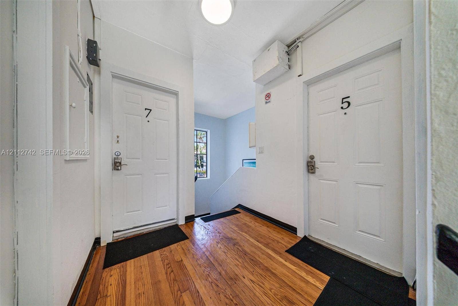 7124 Bay Drive, Miami Beach, FL 33141 Common area featuring wood-finish flooring, two six-panel entry doors, flush-mount ceiling lighting, and a windowed staircase