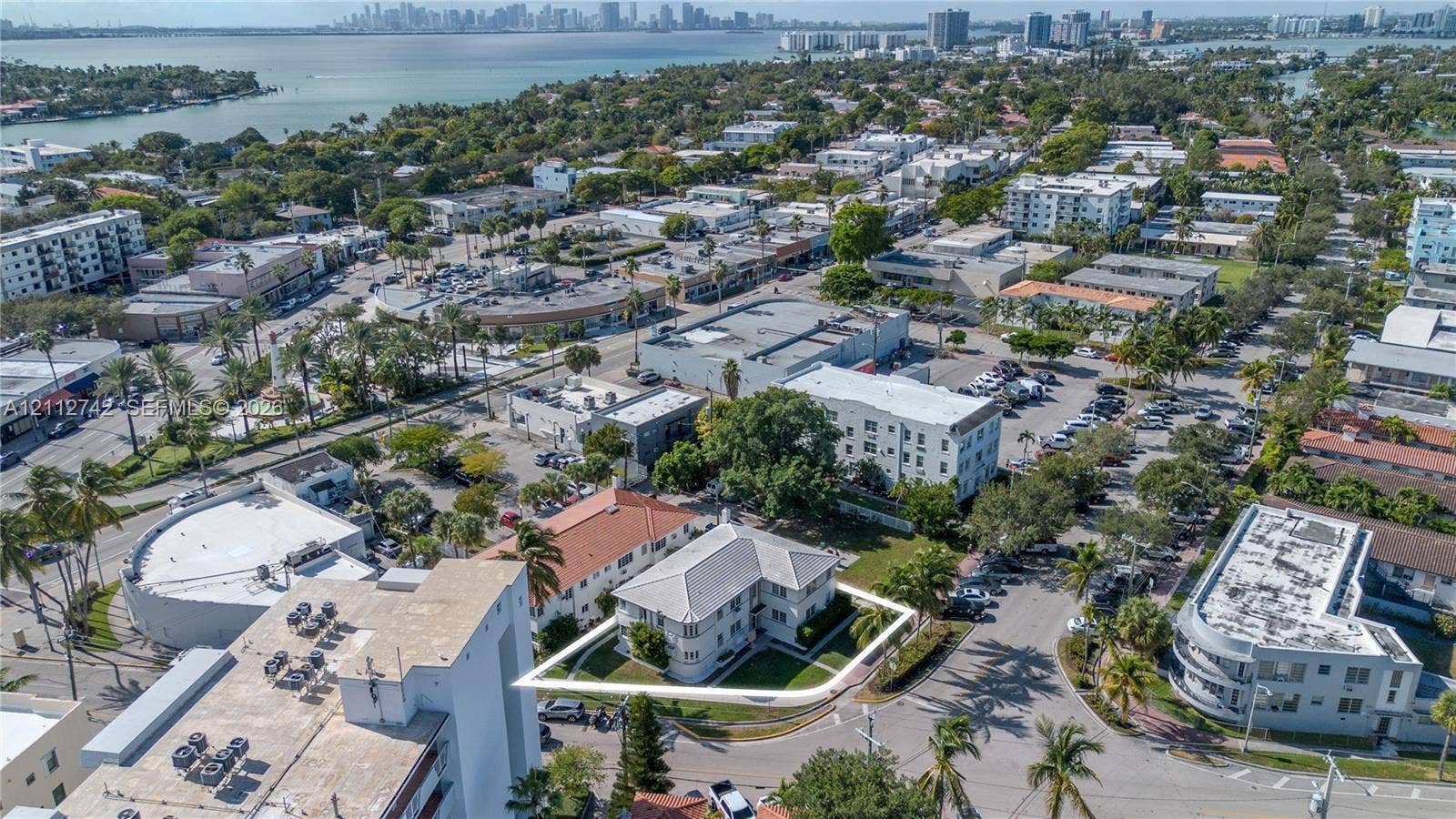 7124 Bay Drive, Miami Beach, FL 33141 Aerial perspective of a multi-story property featuring a hip roof, exterior masonry construction, surrounding lawn space, and mature perimeter trees