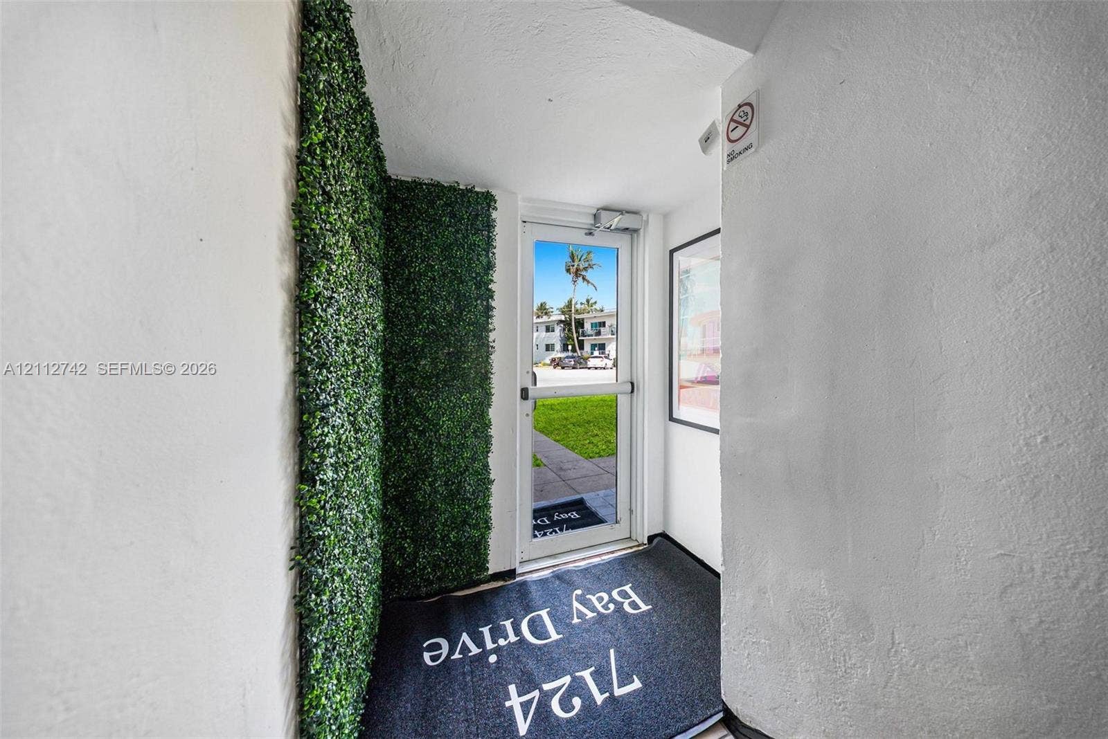 7124 Bay Drive, Miami Beach, FL 33141 Entryway featuring an artificial green wall accent and a full-glass commercial-style door with a panic bar handle
