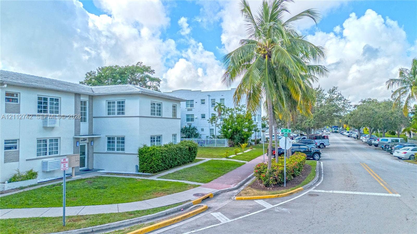 7124 Bay Drive, Miami Beach, FL 33141 Two-story building exterior featuring smooth stucco finish, multi-pane windows, and landscaped grounds with mature palm trees