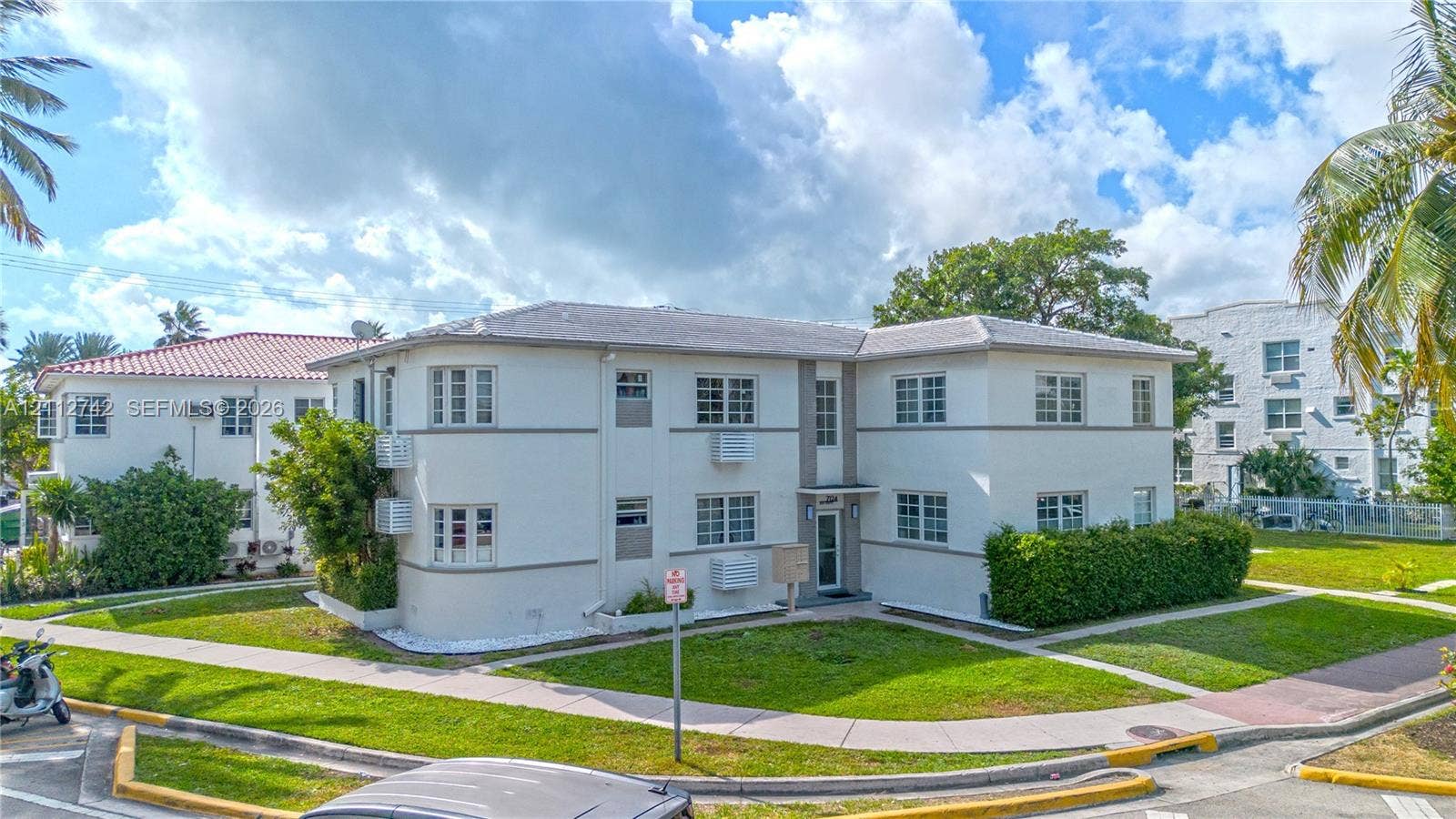 7124 Bay Drive, Miami Beach, FL 33141 Two-story multi-family exterior featuring light-toned stucco walls, a rounded architectural corner, a neutral-toned hip roof, and grid-pane windows