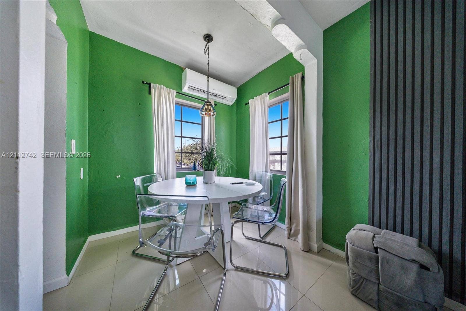 7124 Bay Drive, Miami Beach, FL 33141 Neutral tile flooring, multi-pane windows, wall-mounted ductless climate control unit, hanging pendant light fixture, and vertical slat accent wall