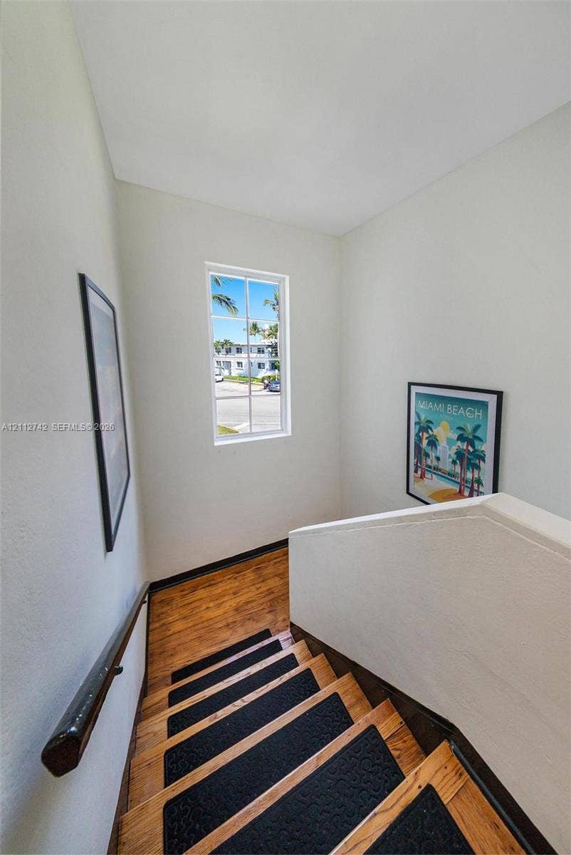 7124 Bay Drive, Miami Beach, FL 33141 Staircase featuring wood-finish treads, contrasting textured inserts, a wall-mounted dark wood handrail, and a vertical window