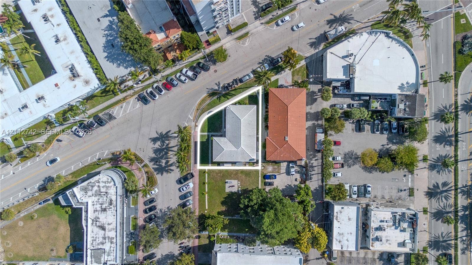 7124 Bay Drive, Miami Beach, FL 33141 Corner lot featuring an L-shaped structure, a light-toned hipped roof, and mature perimeter landscaping
