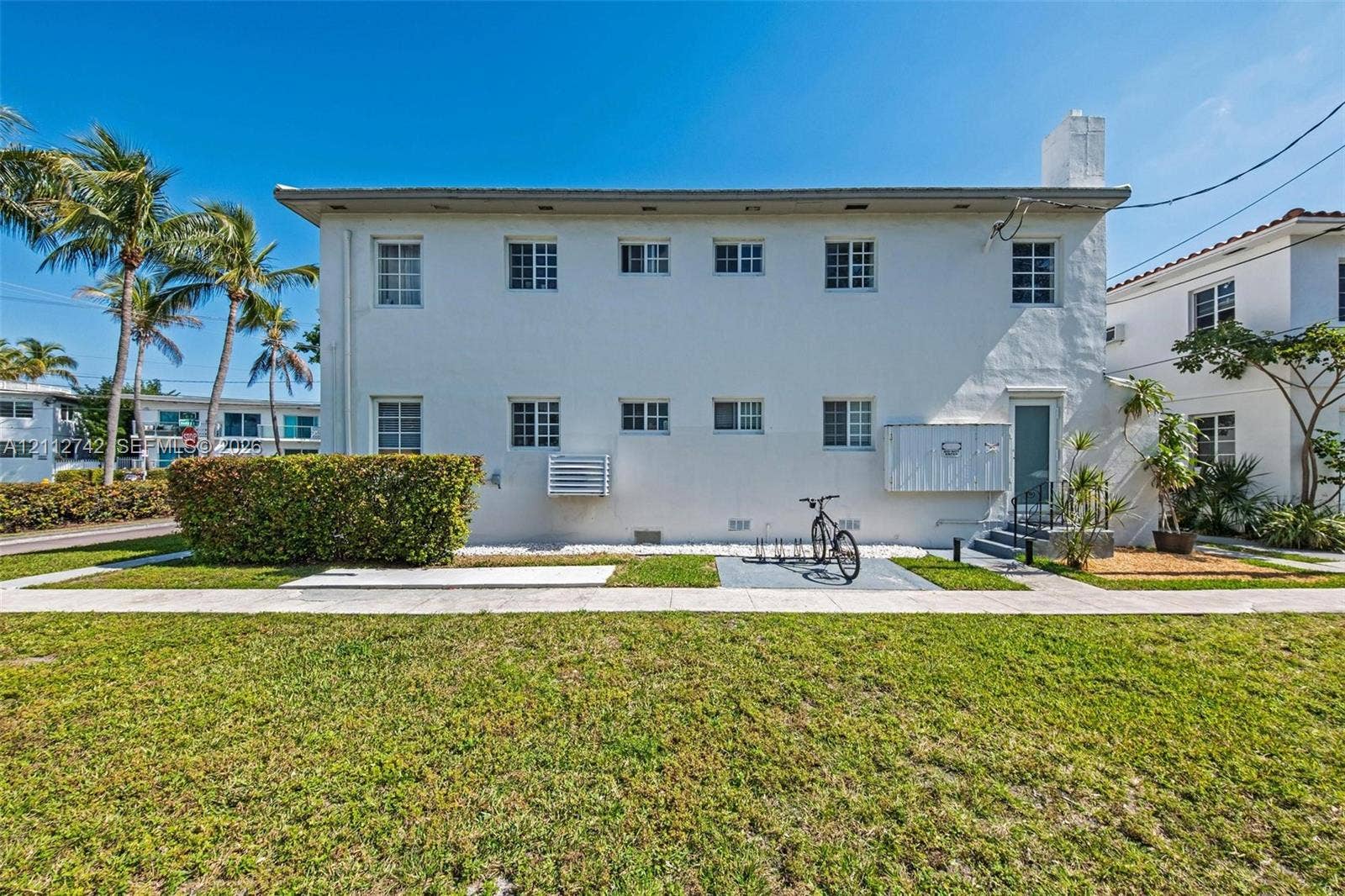 7124 Bay Drive, Miami Beach, FL 33141 Two-story exterior featuring white stucco finish, multi-pane windows, and manicured hedge landscaping