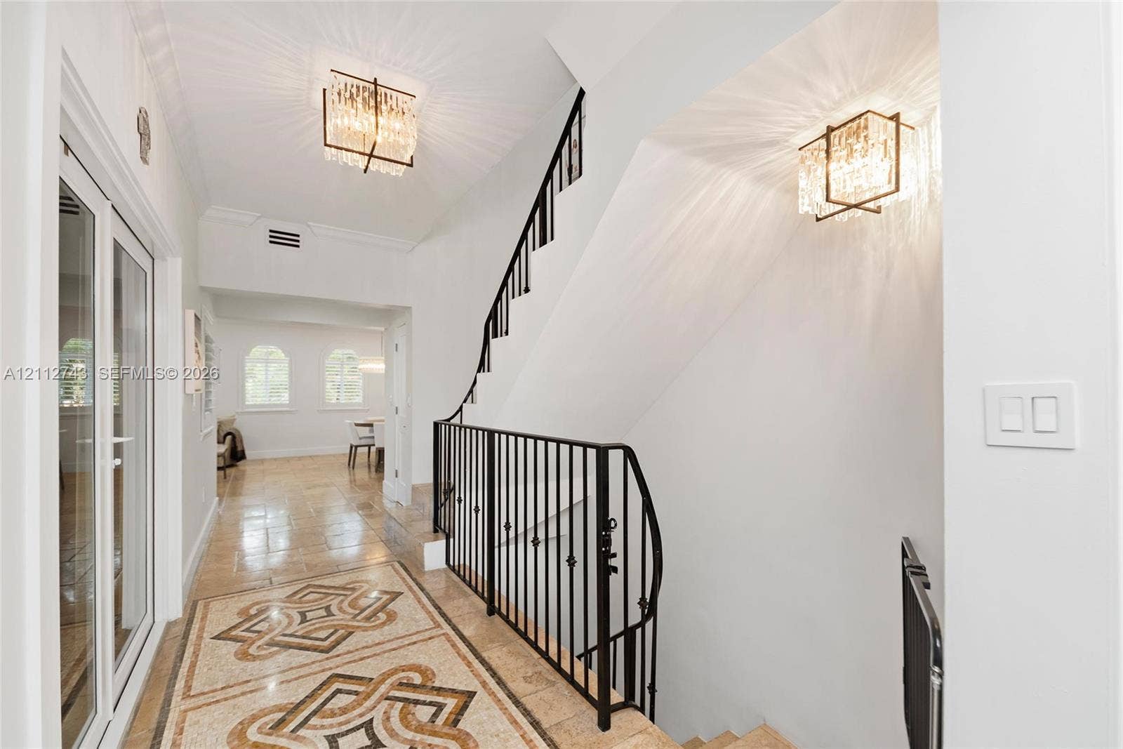 6157 Paradise Point Drive, Palmetto Bay, FL 33157 Foyer featuring intricate stone inlay flooring, black wrought-iron staircase railing, and tiered crystal flush-mount lighting