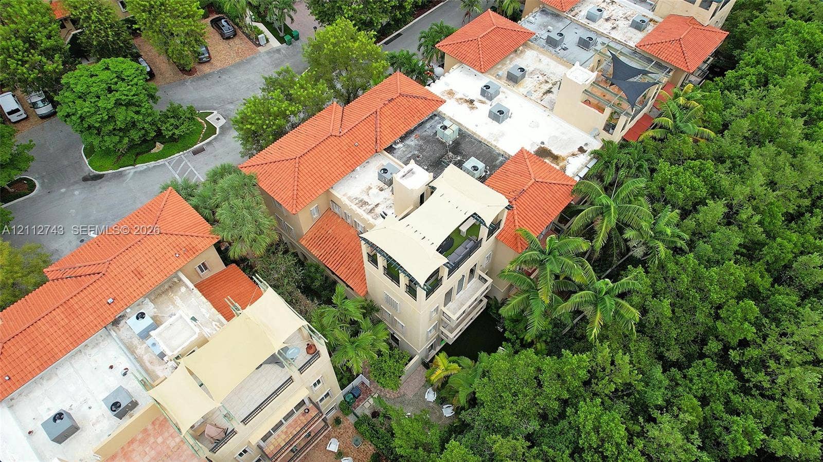 6157 Paradise Point Drive, Palmetto Bay, FL 33157 Aerial perspective featuring multi-story structures with terracotta tile roofing, stucco exteriors, upper-level balconies, and rooftop terraces