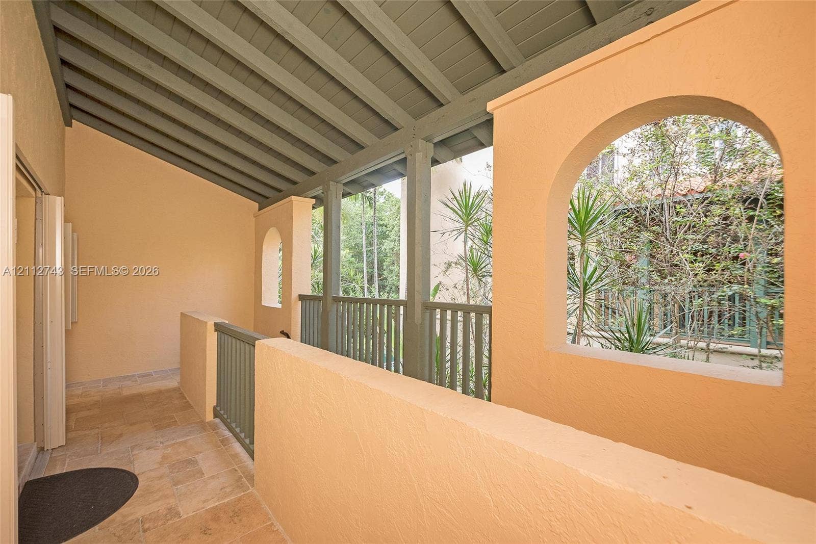 6157 Paradise Point Drive, Palmetto Bay, FL 33157 Covered balcony featuring natural stone flooring, arched openings, exposed ceiling beams, and integrated railing