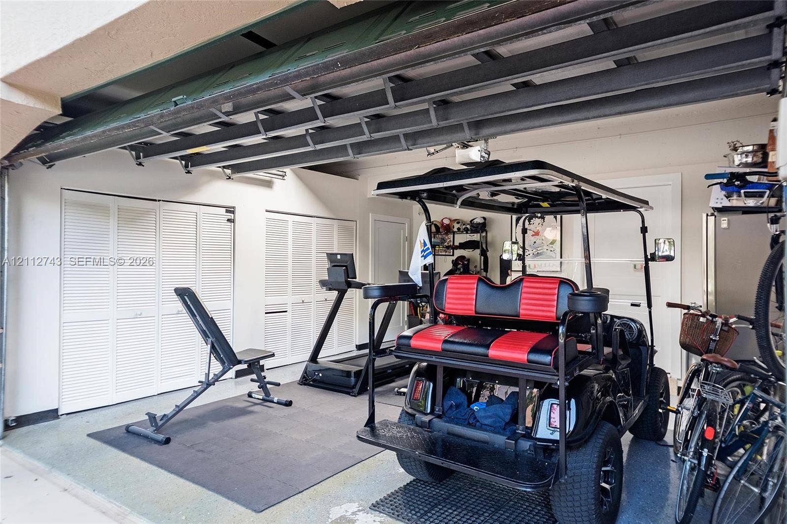 6157 Paradise Point Drive, Palmetto Bay, FL 33157 Garage featuring a dual-track ceiling-mounted door system and multiple sets of white louvered-door built-in storage closets
