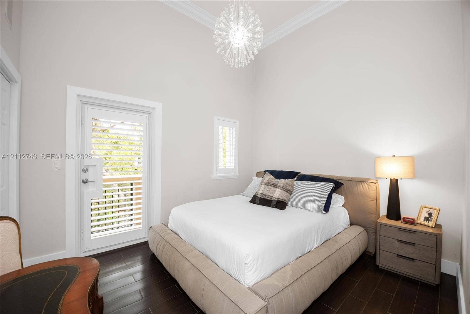 6157 Paradise Point Drive, Palmetto Bay, FL 33157 High-ceiling room featuring dark wood-finish flooring, crown molding, a multi-faceted crystal-style pendant light, and a door with integrated shuttered glass