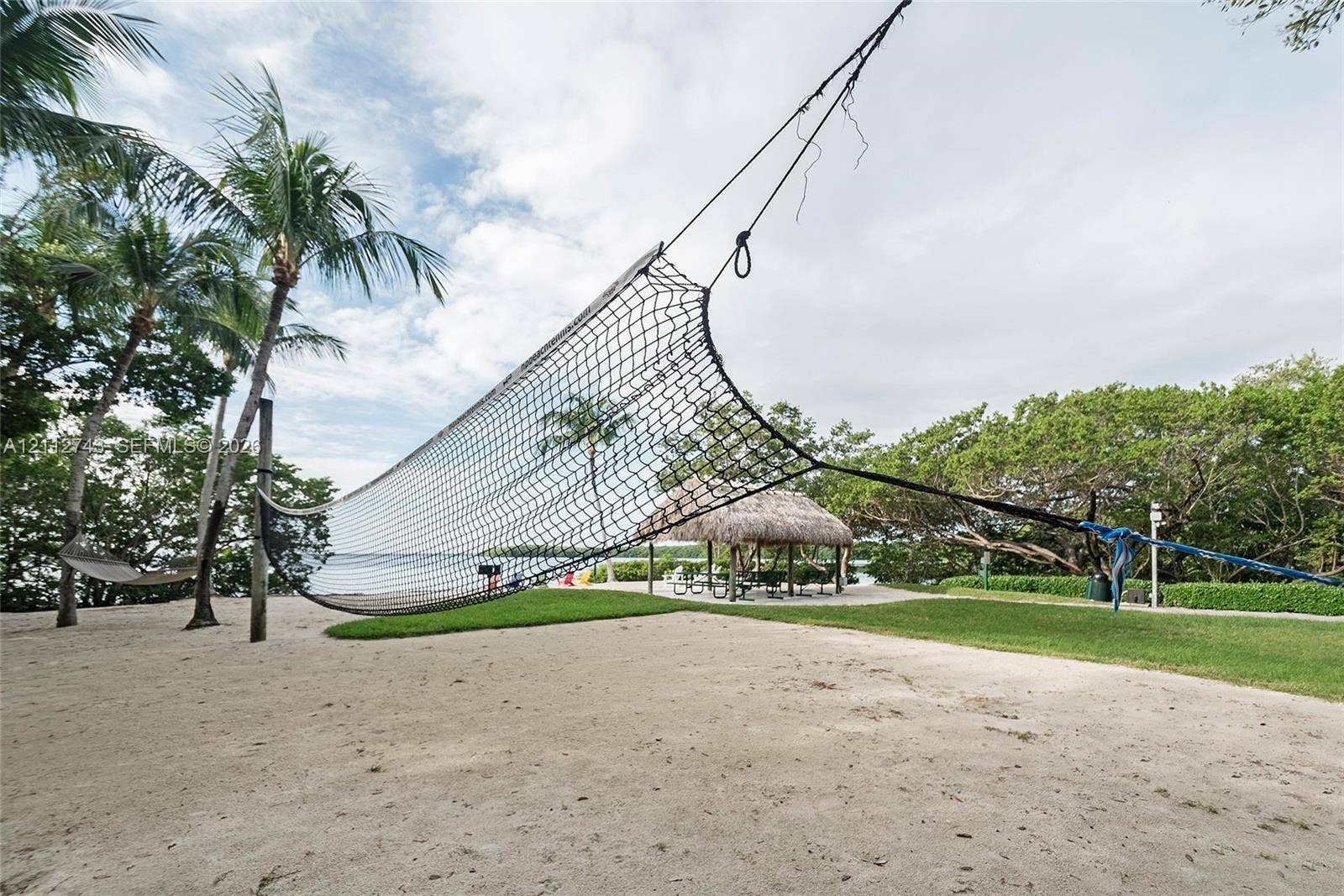 6157 Paradise Point Drive, Palmetto Bay, FL 33157 Sandy outdoor recreation area featuring a volleyball net, grass lawn, thatch-roofed gazebo, and mature palm trees