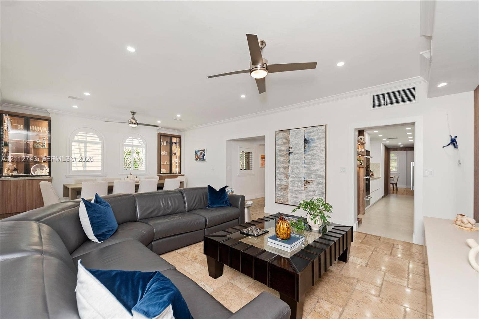 6157 Paradise Point Drive, Palmetto Bay, FL 33157 Open-concept interior featuring natural stone flooring, recessed lighting, ceiling fans, arched windows, and built-in cabinetry with glass-front display shelves