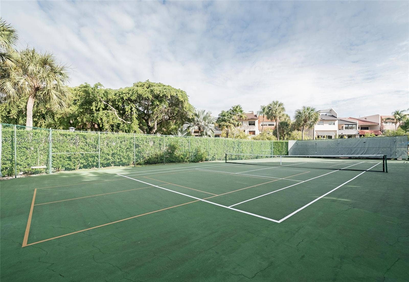 6157 Paradise Point Drive, Palmetto Bay, FL 33157 Private tennis/pickleball court featuring a green surface, perimeter chain-link fencing, and mature landscaping
