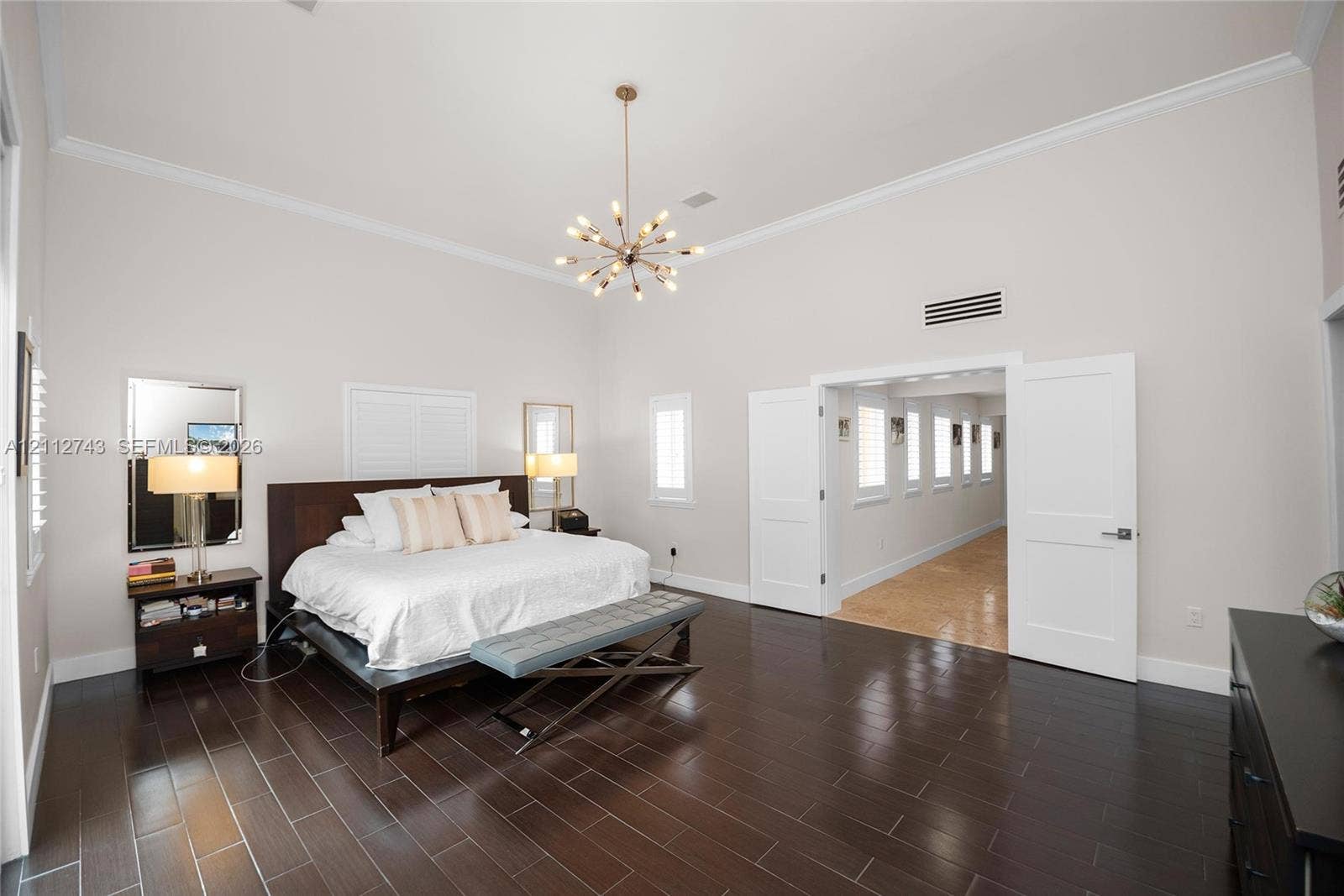 6157 Paradise Point Drive, Palmetto Bay, FL 33157 High-ceilinged room featuring dark wood-finish tile flooring, crown molding, multi-light metallic chandelier, and double doors opening to a secondary space