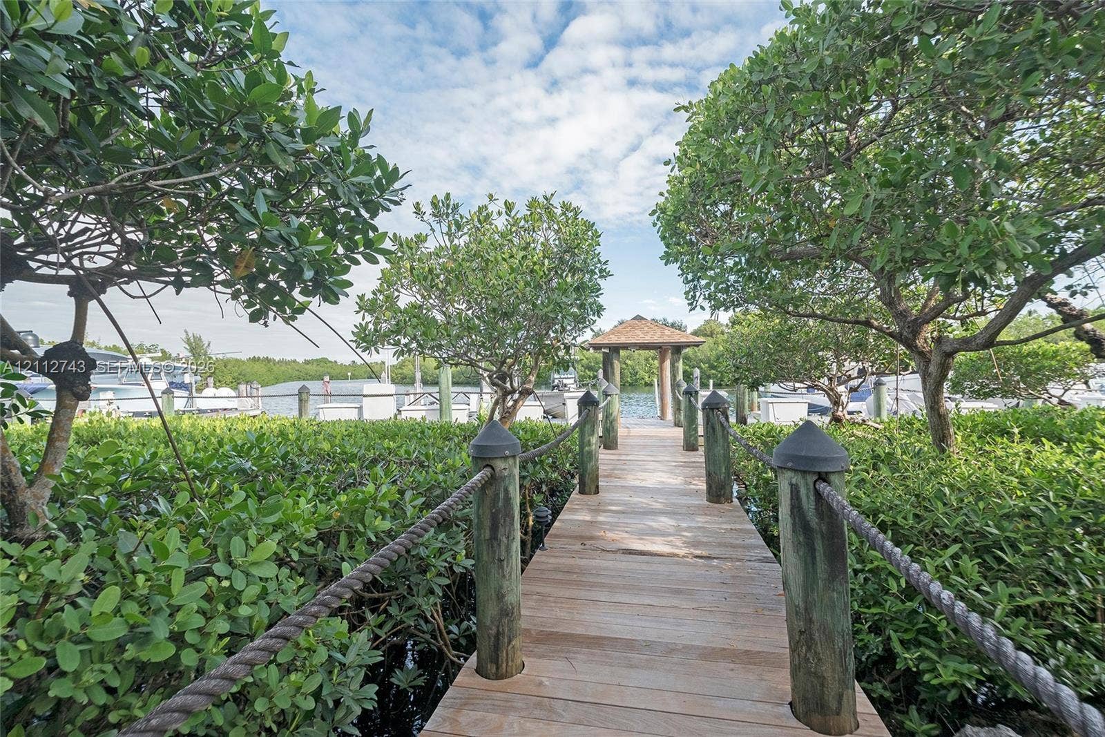 6157 Paradise Point Drive, Palmetto Bay, FL 33157 Wood-plank dock featuring post-and-rope railings, a covered gazebo terminal, and mature vegetation