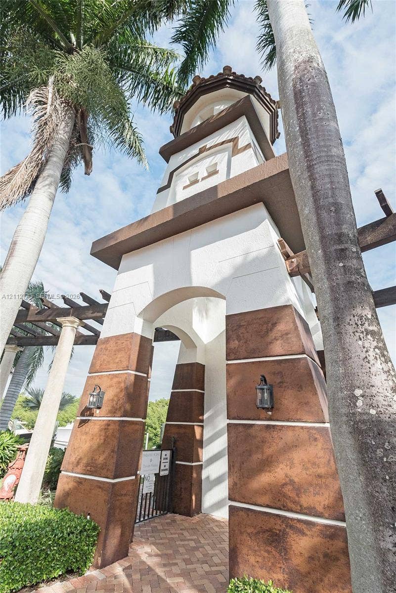 6157 Paradise Point Drive, Palmetto Bay, FL 33157 Architectural tower featuring a stucco exterior, decorative stone-finish base, arched entryway, and attached lantern-style lighting fixtures, set atop a paver walkway