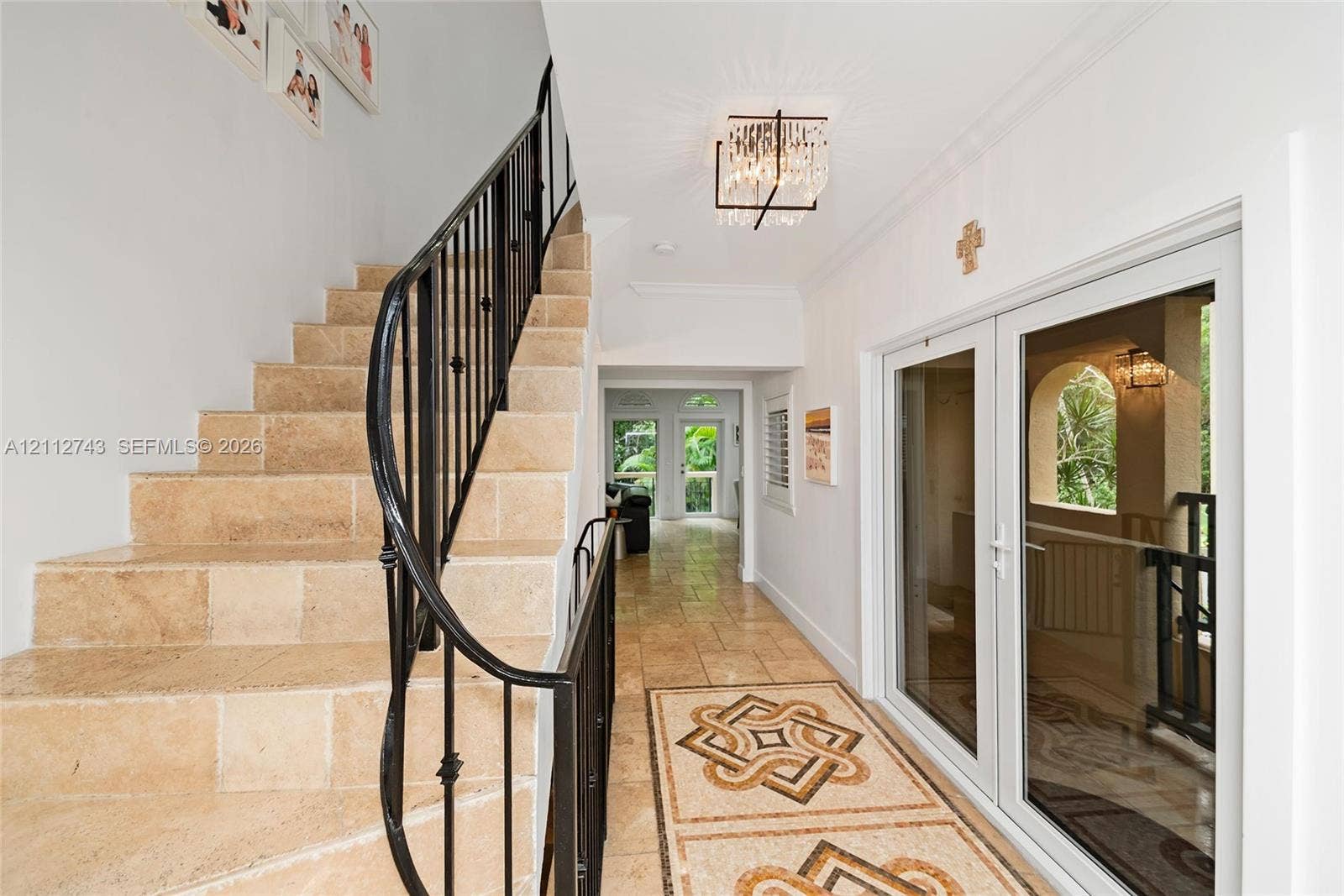 6157 Paradise Point Drive, Palmetto Bay, FL 33157 Foyer featuring stone tile flooring with decorative geometric inlay, a custom wrought-iron staircase railing, and a tiered crystal chandelier