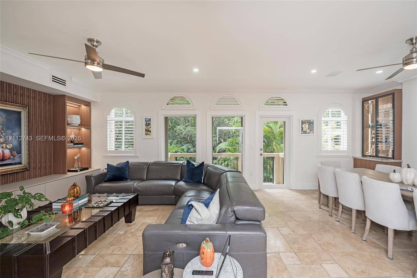 6157 Paradise Point Drive, Palmetto Bay, FL 33157 Open living space featuring stone flooring, arched windows, recessed lighting, built-in wooden display shelving, and dual ceiling fans