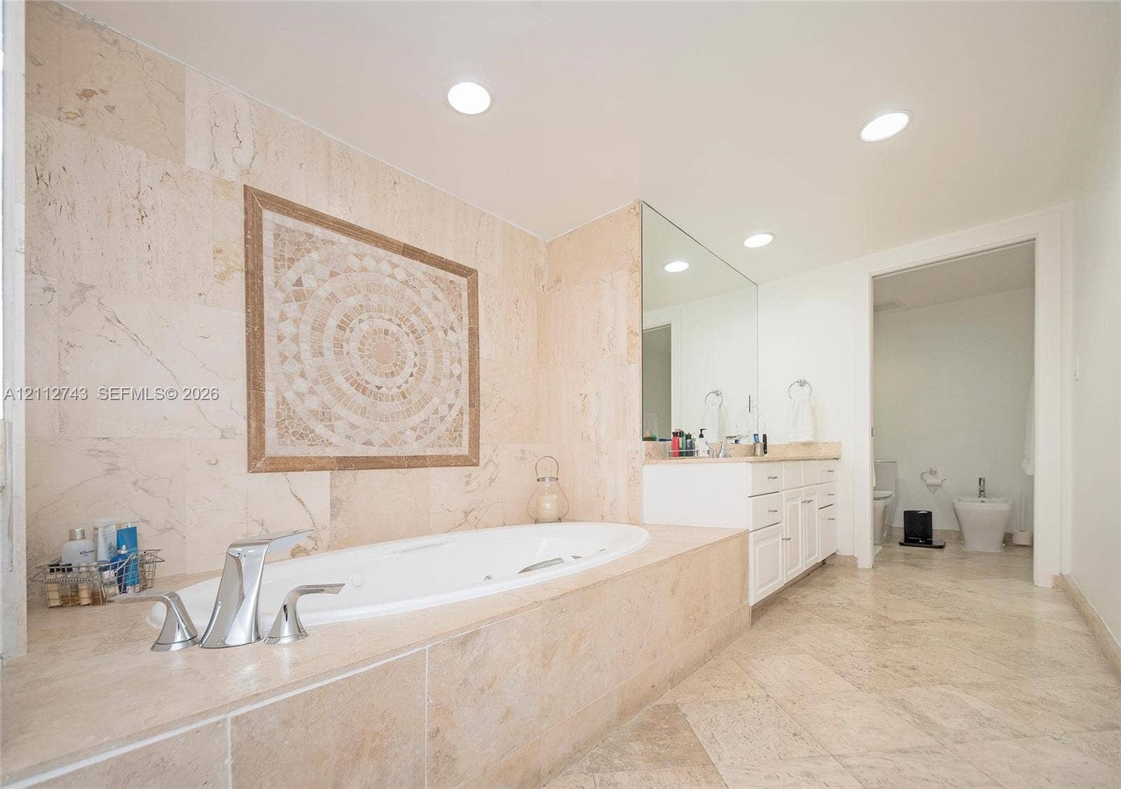 6157 Paradise Point Drive, Palmetto Bay, FL 33157 Stone-tiled soaking tub surround with decorative mosaic inlay, recessed lighting, expansive wall-mounted mirror, and stone flooring