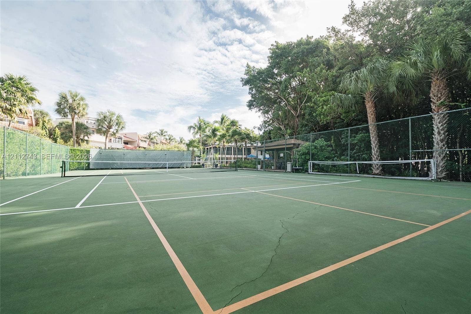 6157 Paradise Point Drive, Palmetto Bay, FL 33157 Hard-surface tennis court featuring perimeter chain-link fencing, a integrated net system, and surrounding mature palm trees