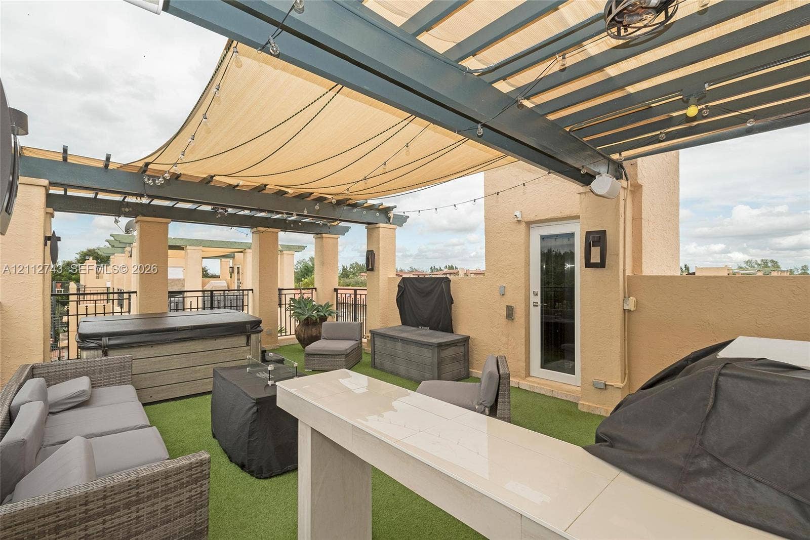 6157 Paradise Point Drive, Palmetto Bay, FL 33157 Rooftop terrace featuring a custom metal pergola with integrated shade canopy, built-in bar, artificial turf flooring, and a recessed spa
