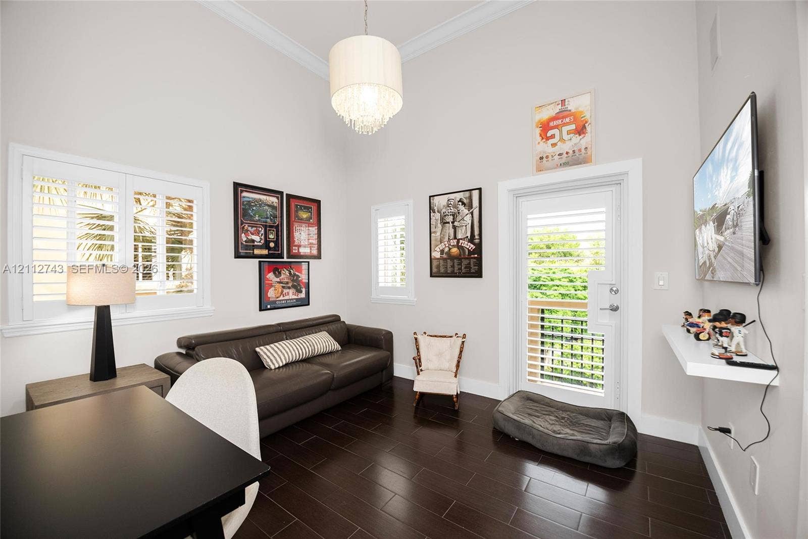 6157 Paradise Point Drive, Palmetto Bay, FL 33157 Vaulted ceilings, dark wood-finish flooring, plantation shutters, a multi-tiered crystal pendant light fixture, and a glass-paneled exterior door