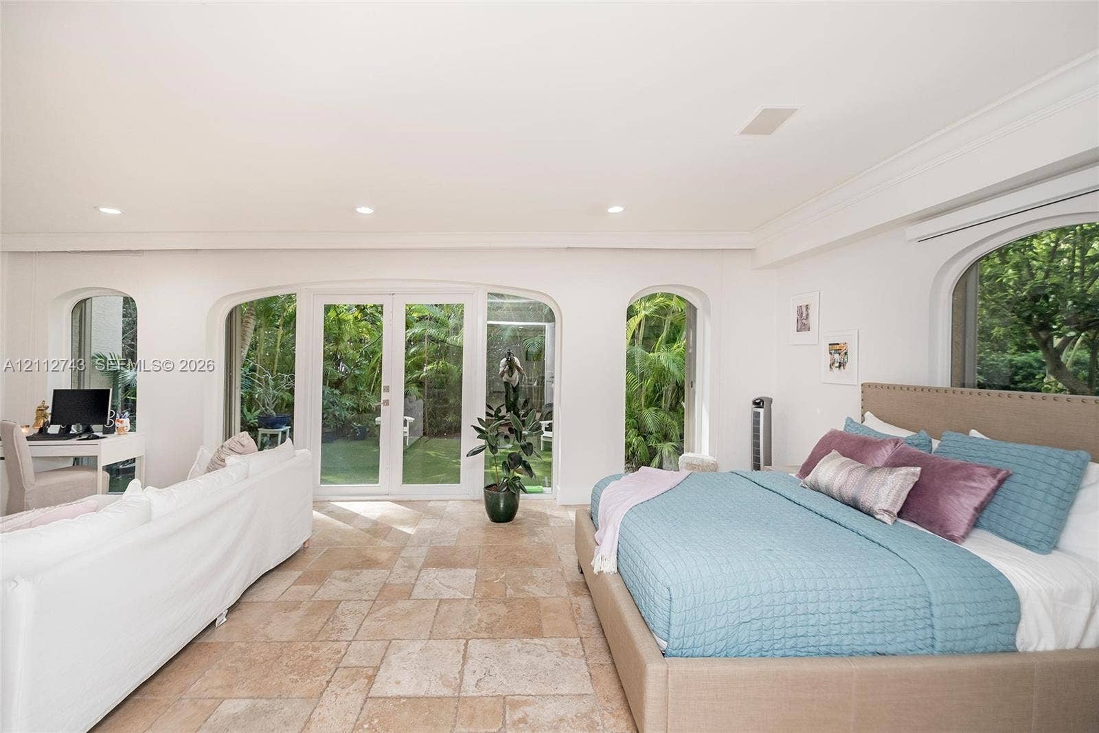 6157 Paradise Point Drive, Palmetto Bay, FL 33157 Spacious room featuring light stone-finish tile flooring, arched window casings, crown molding, and glass-paneled double doors providing outdoor access