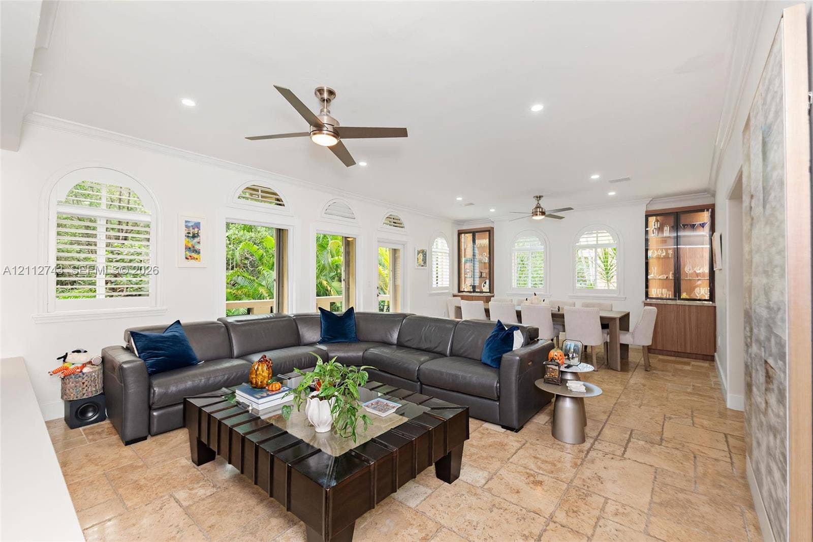 6157 Paradise Point Drive, Palmetto Bay, FL 33157 Open-concept interior featuring large-format tile flooring, multiple arched windows with built-in shutters, dual ceiling fans, and integrated custom cabinetry