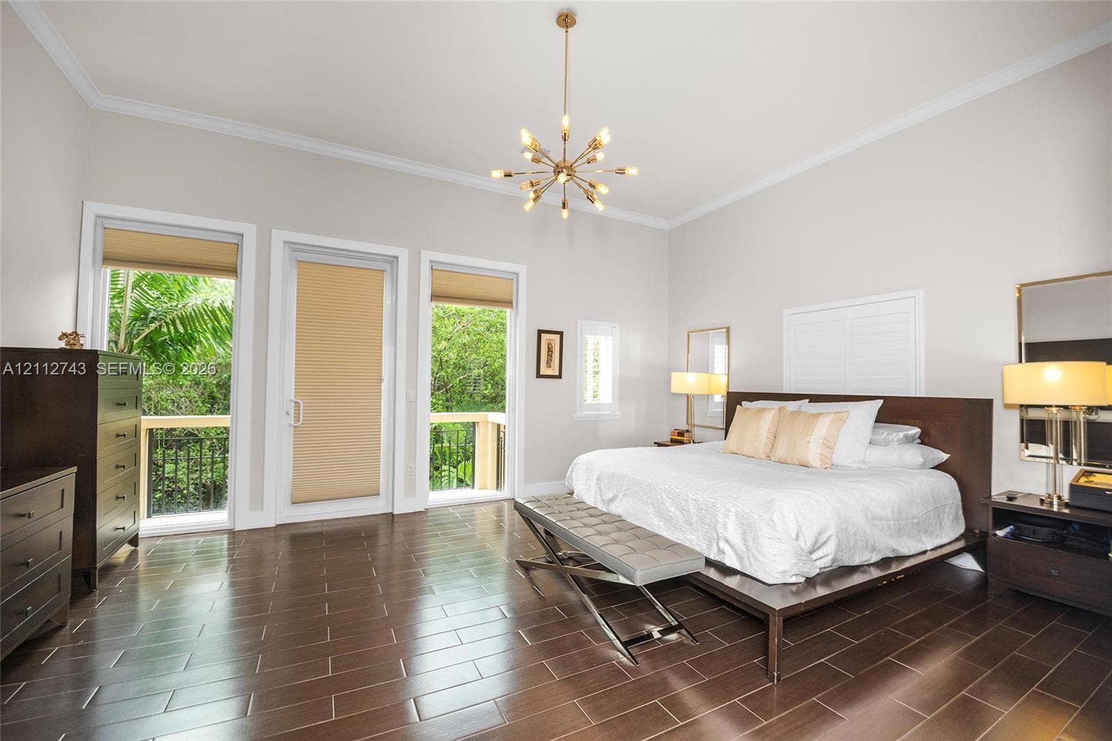 6157 Paradise Point Drive, Palmetto Bay, FL 33157 Spacious room featuring wood-finish tile flooring, crown molding, a central multi-arm chandelier, and two glass-panel doors leading to an exterior balcony