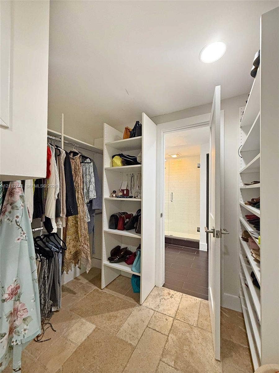 6157 Paradise Point Drive, Palmetto Bay, FL 33157 Walk-in closet featuring custom white built-in shelving, hanging rods, and natural stone tile flooring