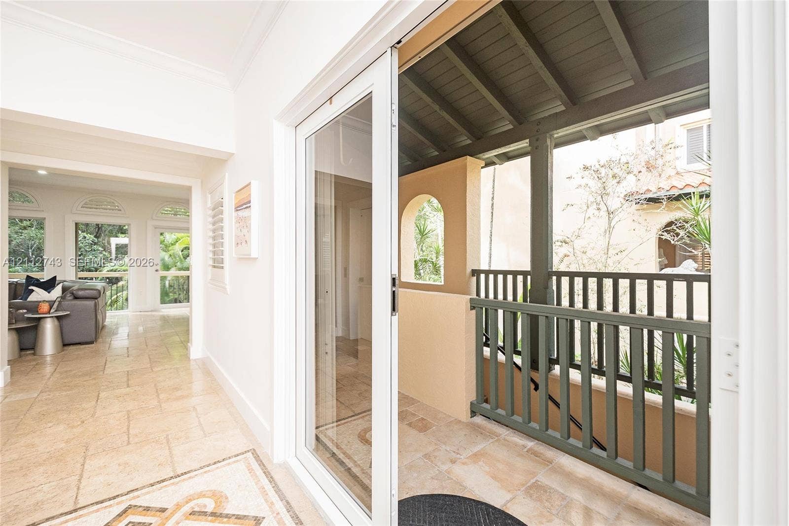 6157 Paradise Point Drive, Palmetto Bay, FL 33157 Covered balcony featuring stone tile flooring and a vertical balustrade, accessed through full-height sliding glass doors