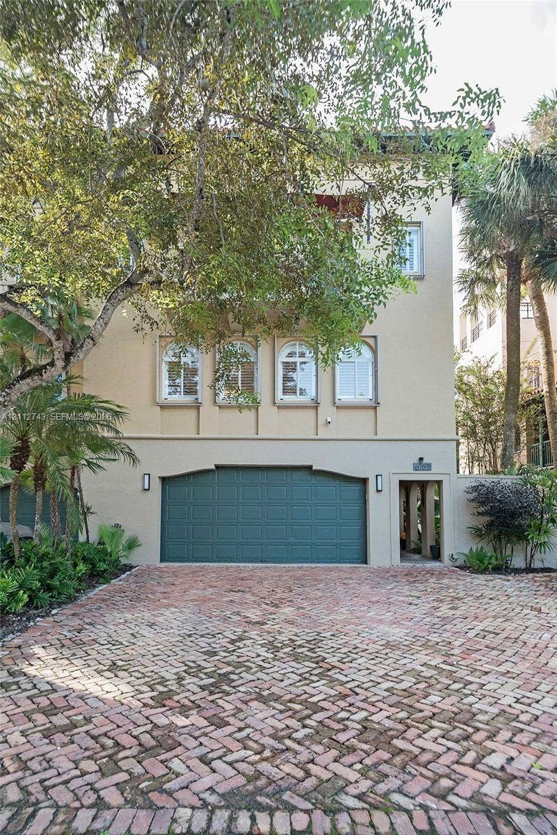 6157 Paradise Point Drive, Palmetto Bay, FL 33157 Stucco exterior featuring arched windows, a multi-level silhouette, a dedicated garage, and a brick-paved driveway