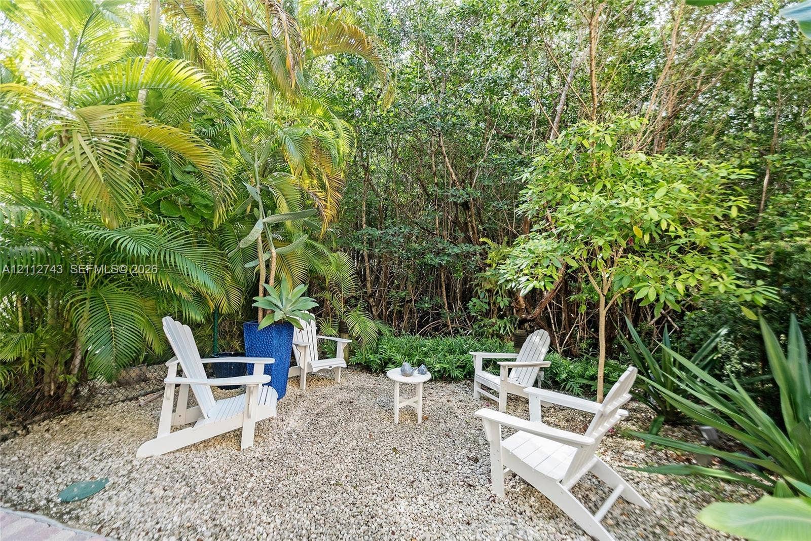 6157 Paradise Point Drive, Palmetto Bay, FL 33157 Gravel patio area featuring mature tropical palms and dense perimeter greenery