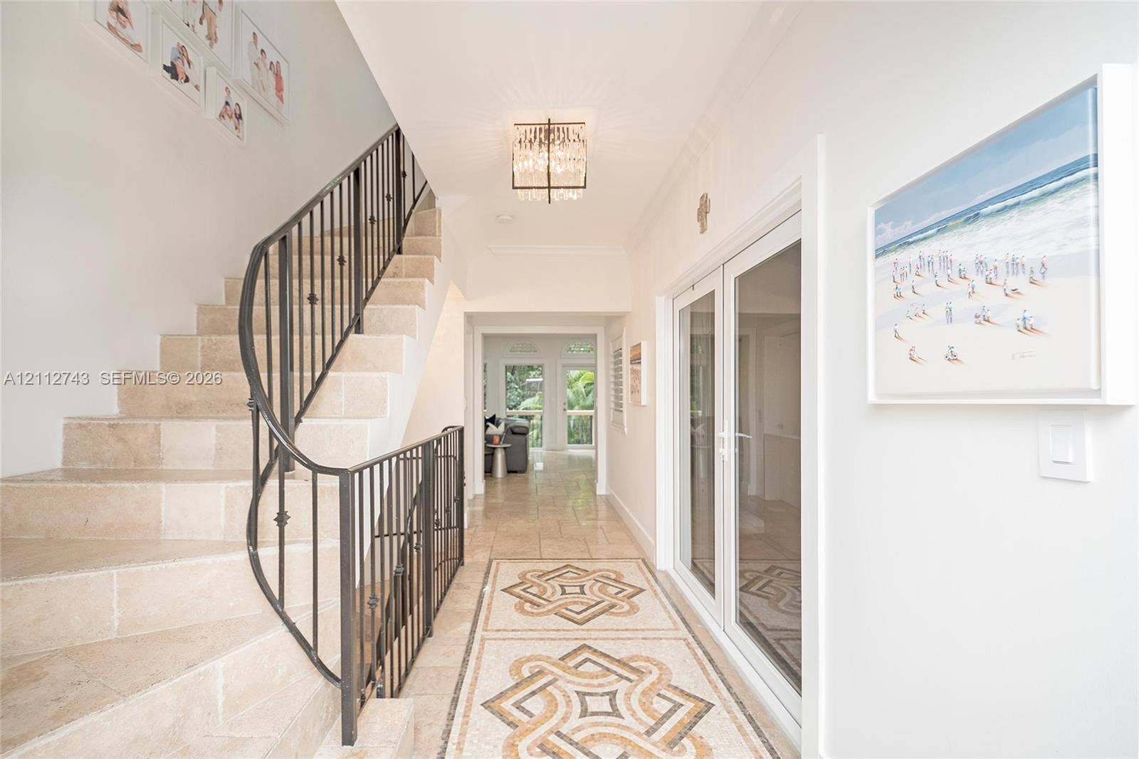6157 Paradise Point Drive, Palmetto Bay, FL 33157 Foyer featuring stone stair treads, a decorative metal balustrade, intricate mosaic tile flooring inlay, and a flush-mount crystal chandelier
