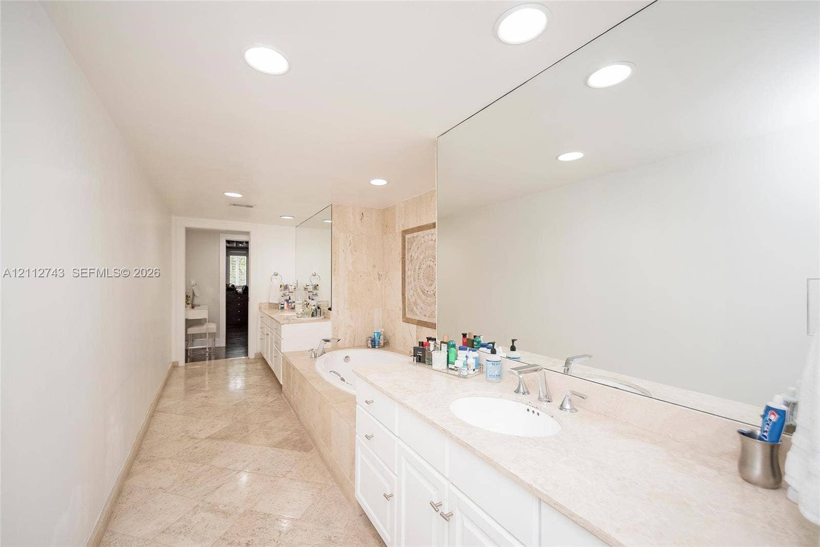 6157 Paradise Point Drive, Palmetto Bay, FL 33157 Bathroom featuring stone-finish flooring, a jetted soaking tub with a tiled surround, a lengthy stone-surface vanity with dual integrated sinks, and expansive wall-to-wall mirrors