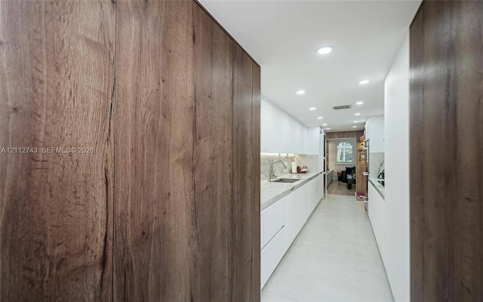 6157 Paradise Point Drive, Palmetto Bay, FL 33157 Modern kitchen featuring flat-panel white cabinetry, stone-finish countertops, wood-finish paneling, recessed lighting, and under-cabinet illumination