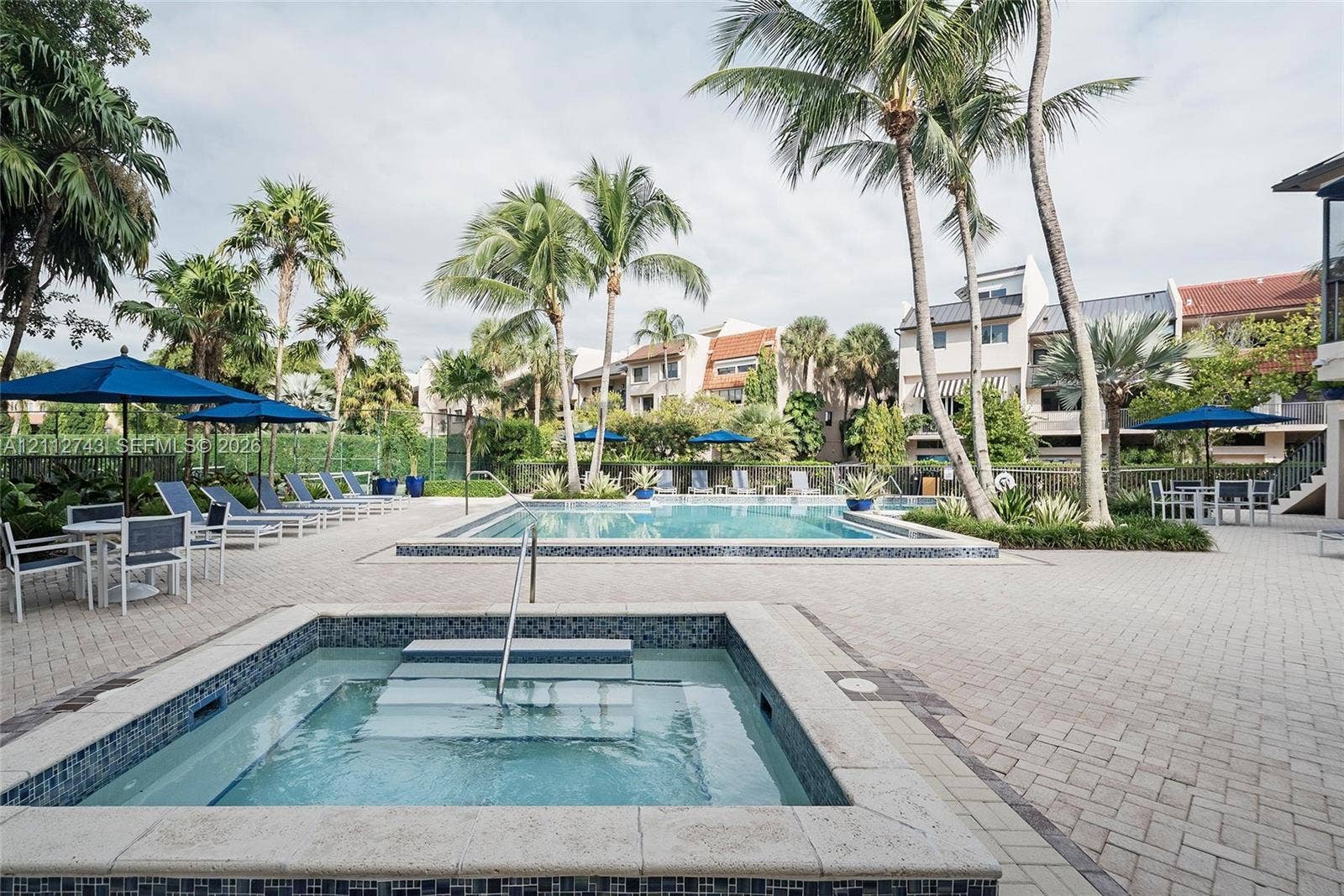 6157 Paradise Point Drive, Palmetto Bay, FL 33157 Outdoor swimming pool and spa featuring a stone-paver deck, built-in steps, and surrounding palm trees