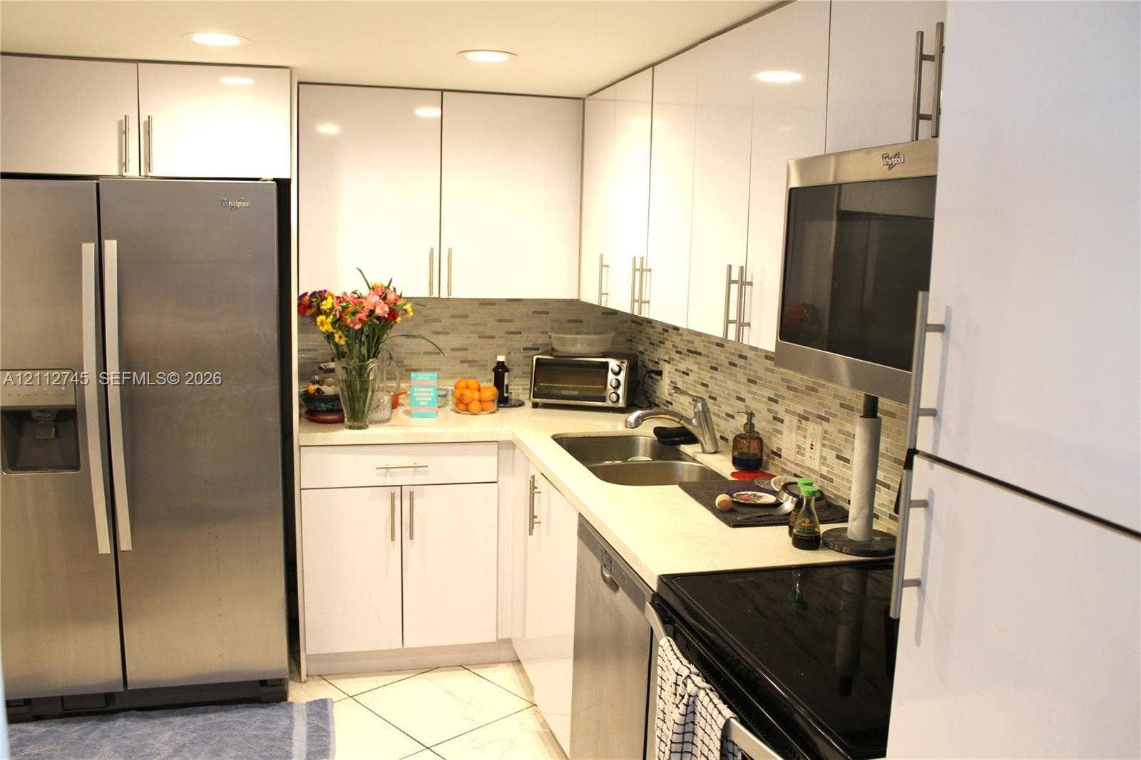 20500 W Country Club Drive, #202, Aventura, FL 33180 Kitchen featuring high-gloss white cabinetry, stainless steel appliances, stone-finish countertops, tile backsplash, and tile flooring